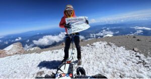 IISc Professor Arpita Patra planting a flag on the snowy summit of a volcanic peak, celebrating her high-altitude climb.