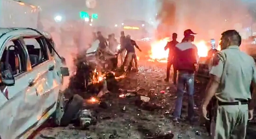 A somber image of the blast site near the Red Fort Metro Station, showing emergency services (police, fire, and ambulance) and the secured-off area.